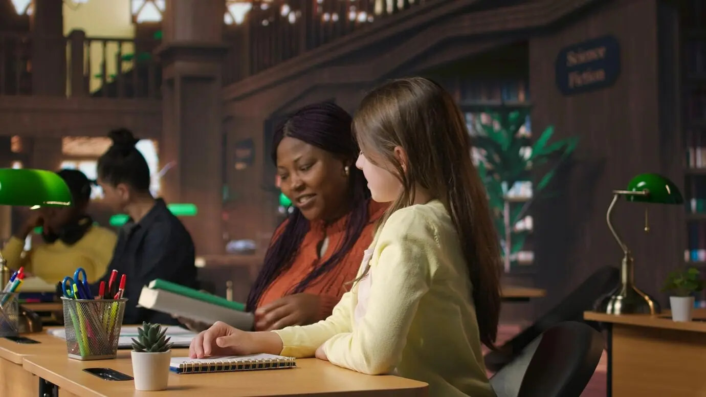 Lehrerin weckt ihren auf dem Arbeitstisch in der Bibliothek schlafenden Schüler.